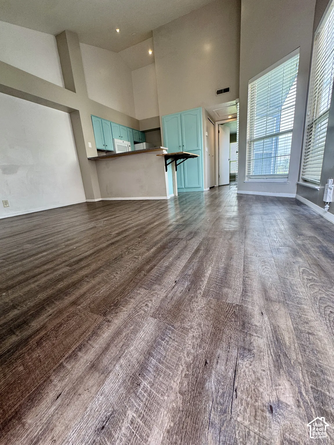 Vaulted ceilings with recessed lighting, wood-finish flooring, kitchen with teal cabinetry, breakfast bar, and white appliances