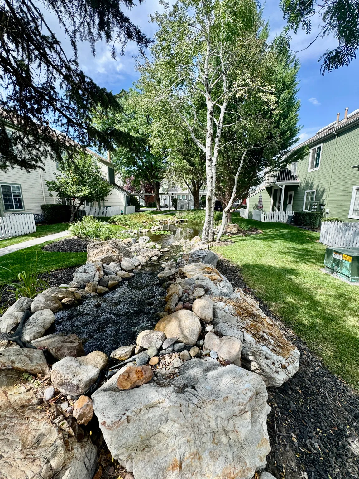 Landscaped water feature with natural rock elements, surrounded by a manicured lawn and mature trees