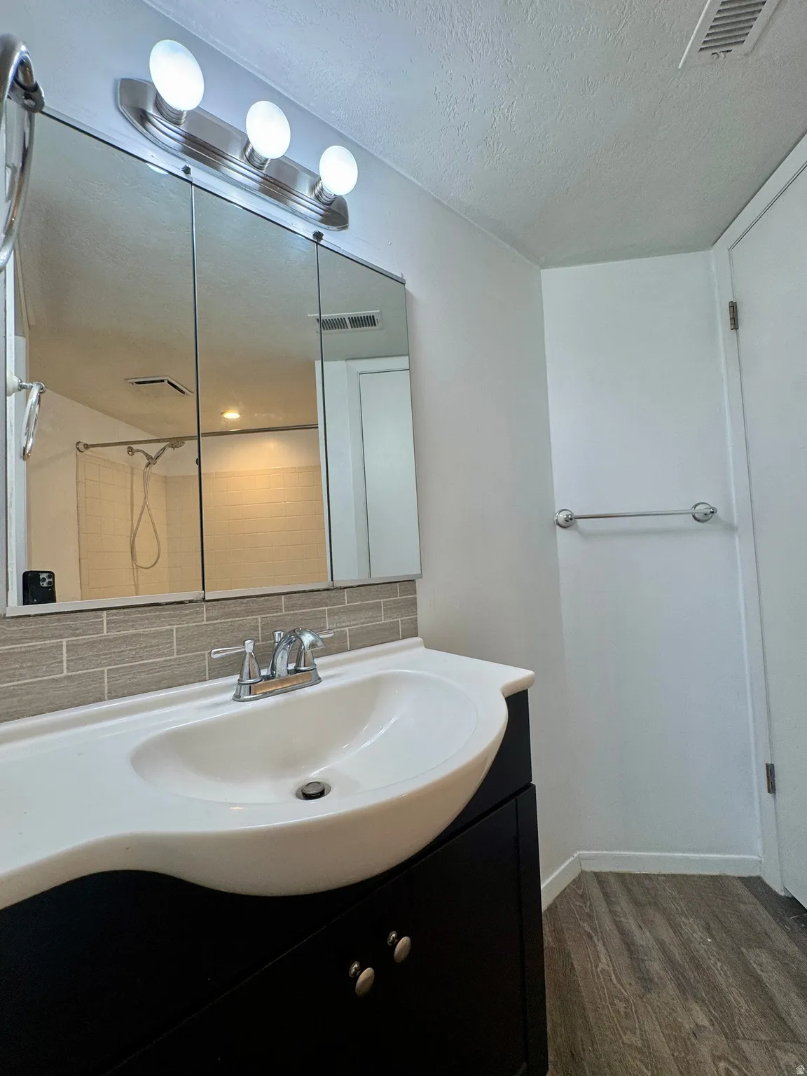 Integrated vanity with a white basin and dark-finish cabinetry, tile backsplash, and wood-finish flooring