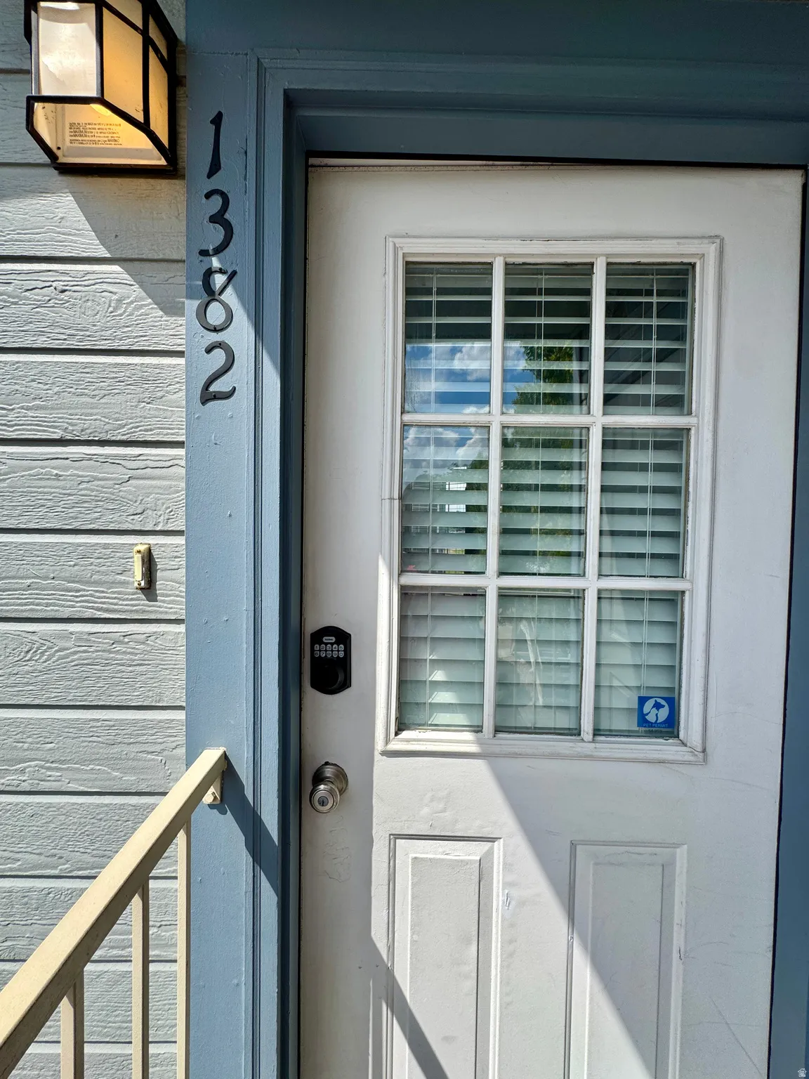 White paneled entry door with multi-pane window, integrated blinds, and keyless entry system