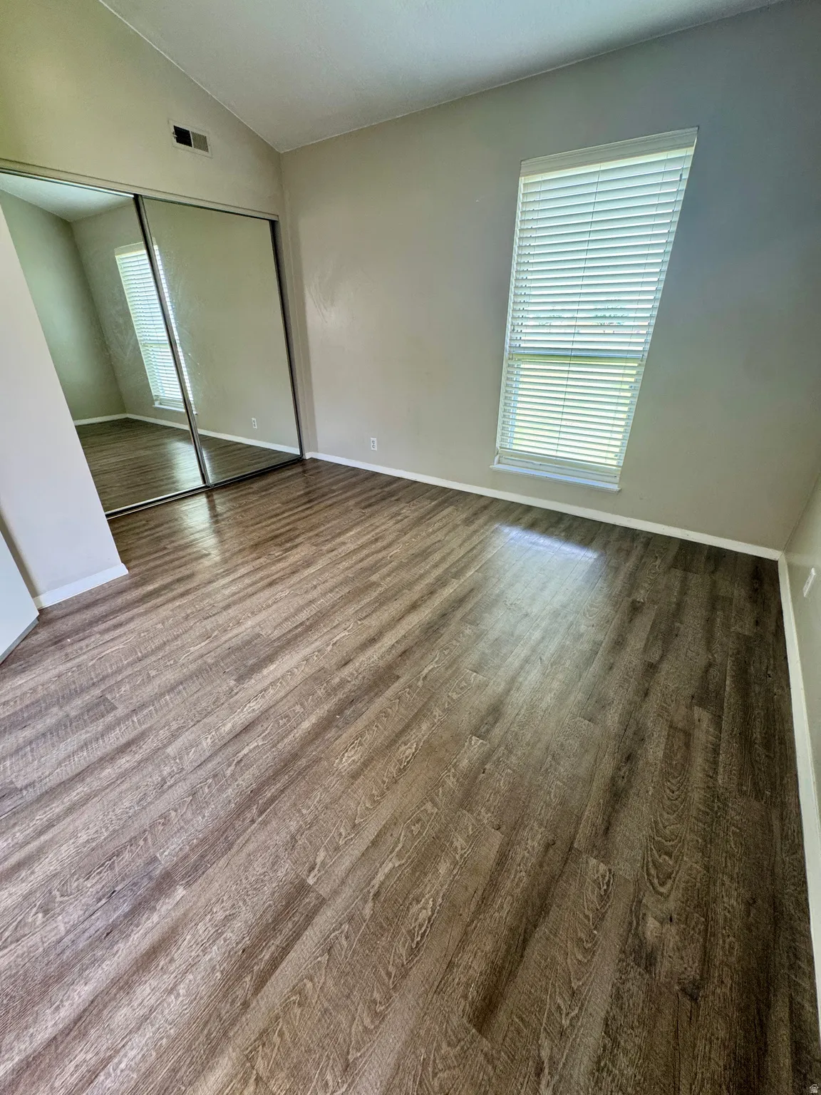 Wood-finish flooring, mirrored closet doors, vaulted ceiling, and a large window with blinds