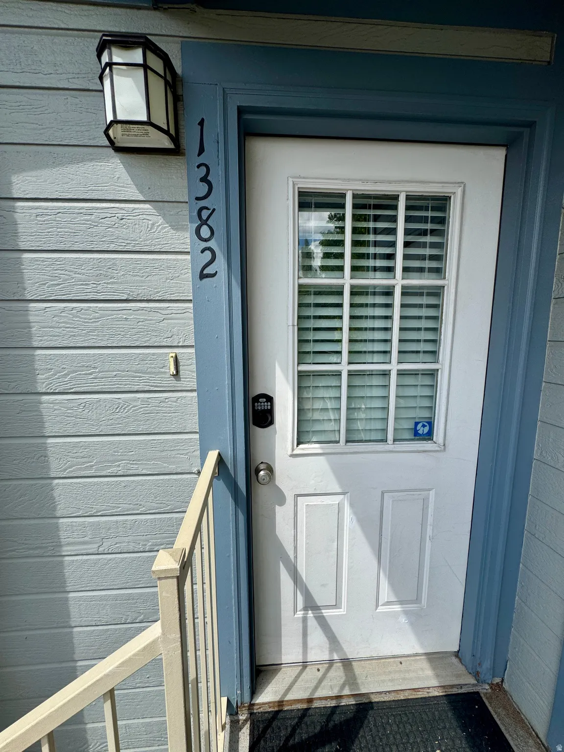 Entry door with upper window panes, digital keypad lock, and exterior light fixture