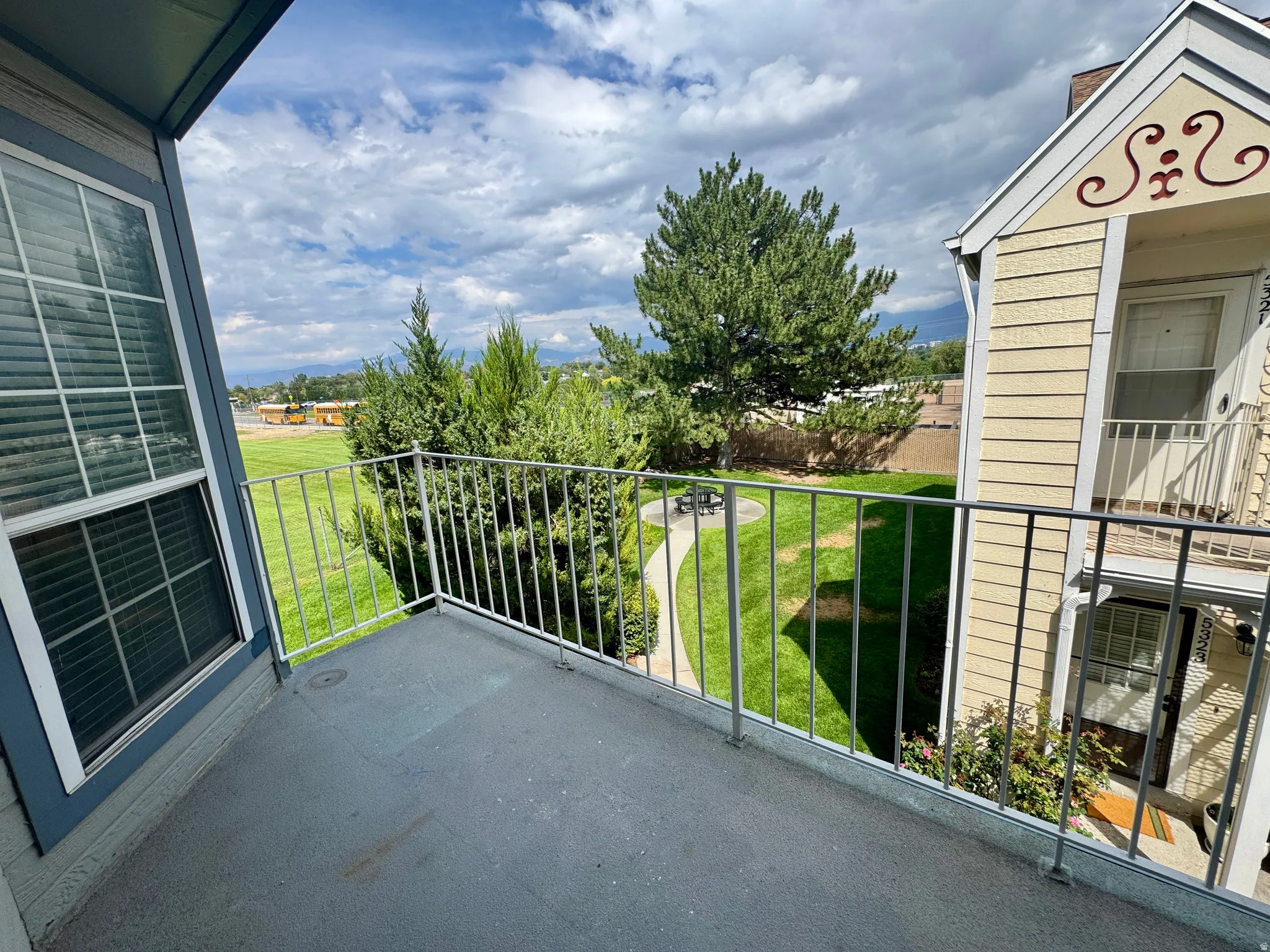 Private balcony with metal railings and a blue-gray floor, offering a green landscape with mature trees