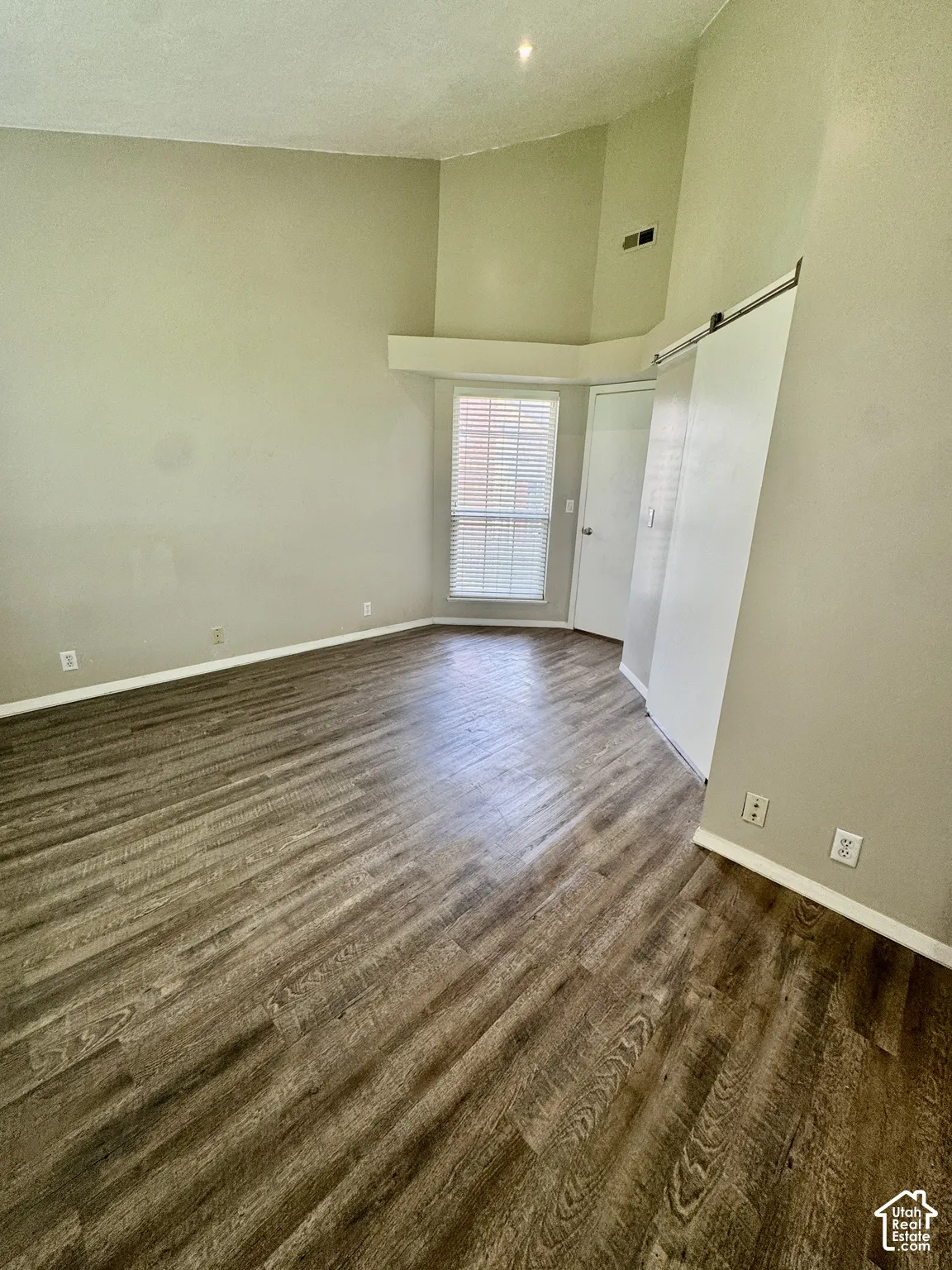 Vaulted ceiling with a wood-finish flooring, featuring a window with blinds and a sliding barn door
