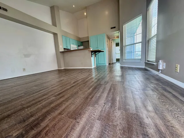 Vaulted ceilings, wood-finish flooring, kitchen with teal cabinetry, and large windows with blinds
