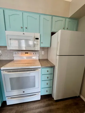 Kitchen featuring light teal cabinetry, white appliances, gray tile backsplash, and wood-finish flooring