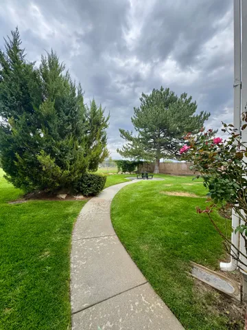 Curved concrete pathway leading to a green lawn area with mature trees and shrubbery