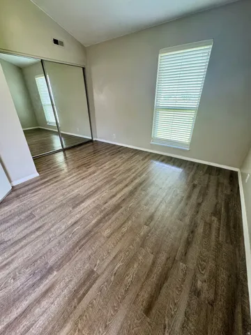 Wood-finish flooring, mirrored closet doors, vaulted ceiling, and a large window with blinds
