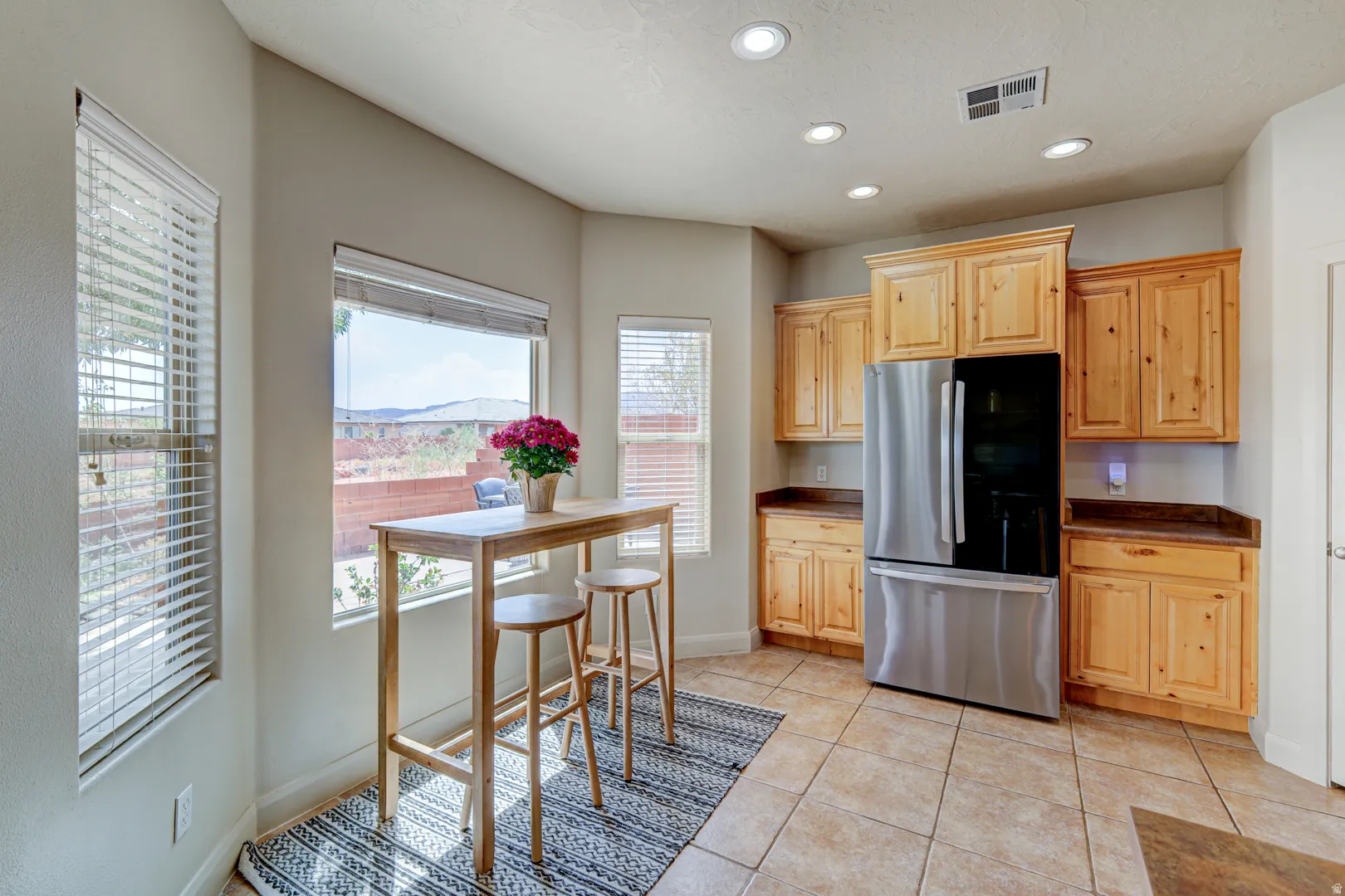 Recessed lighting, wood-finish cabinetry, stainless steel refrigerator, tile flooring, and large window