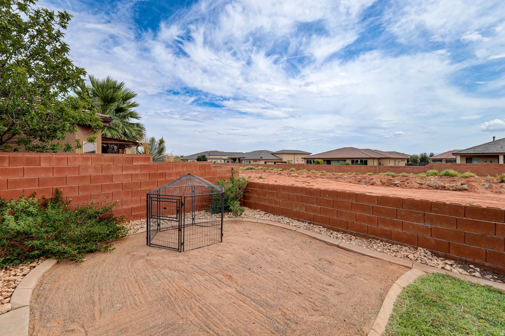 Terraced backyard featuring a red block retaining wall, desert landscaping, and a partial grass area