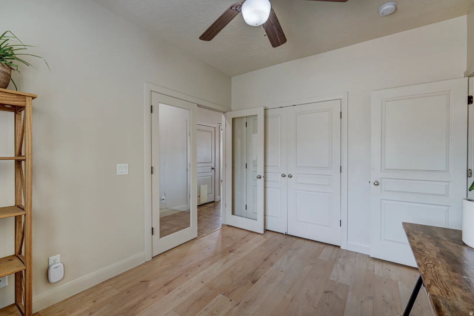 Wood-finish flooring, ceiling fan with integrated lighting, paneled doors, and interior French doors