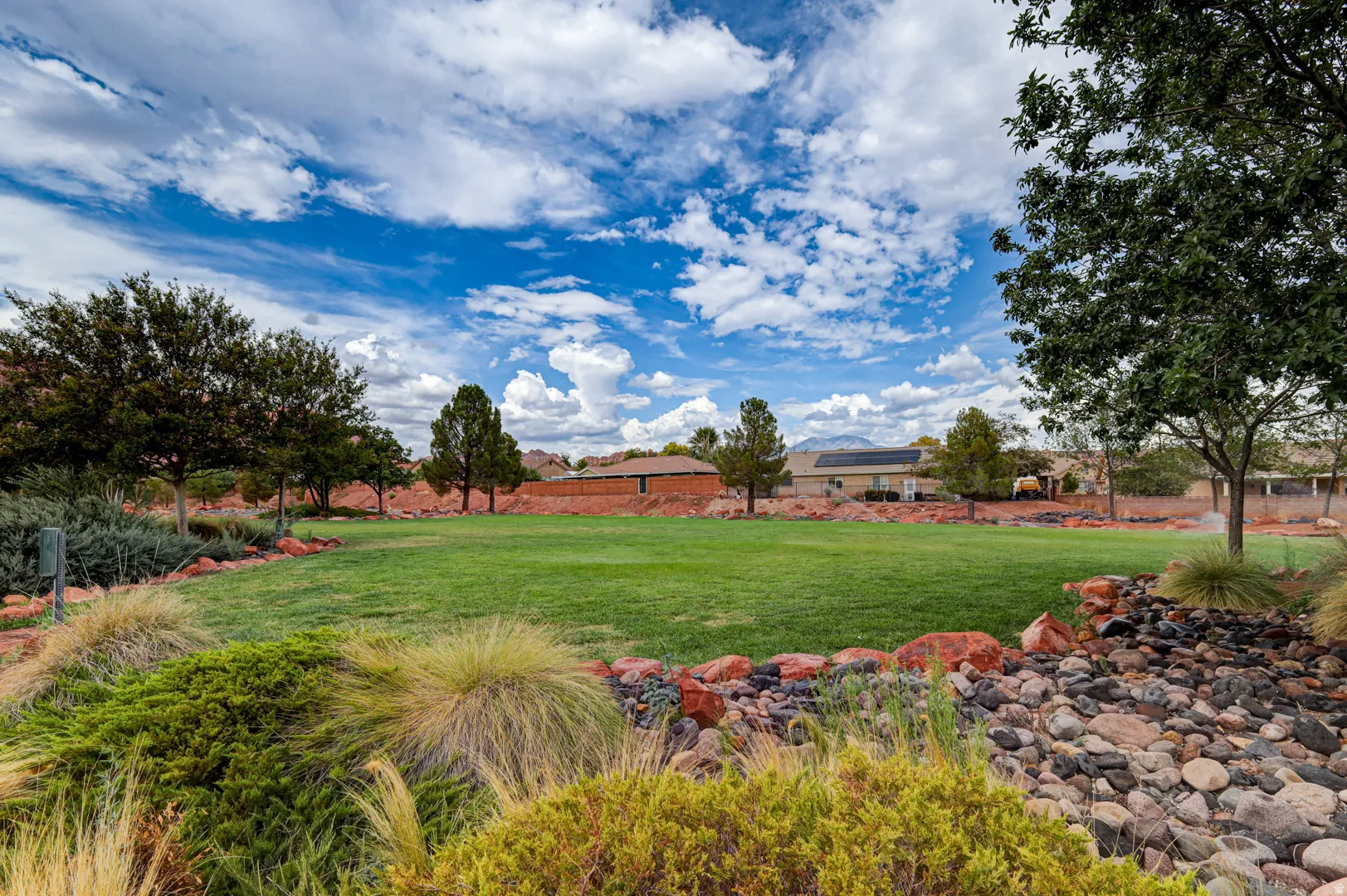 Expansive green space featuring a manicured lawn, established trees, and decorative rock landscaping