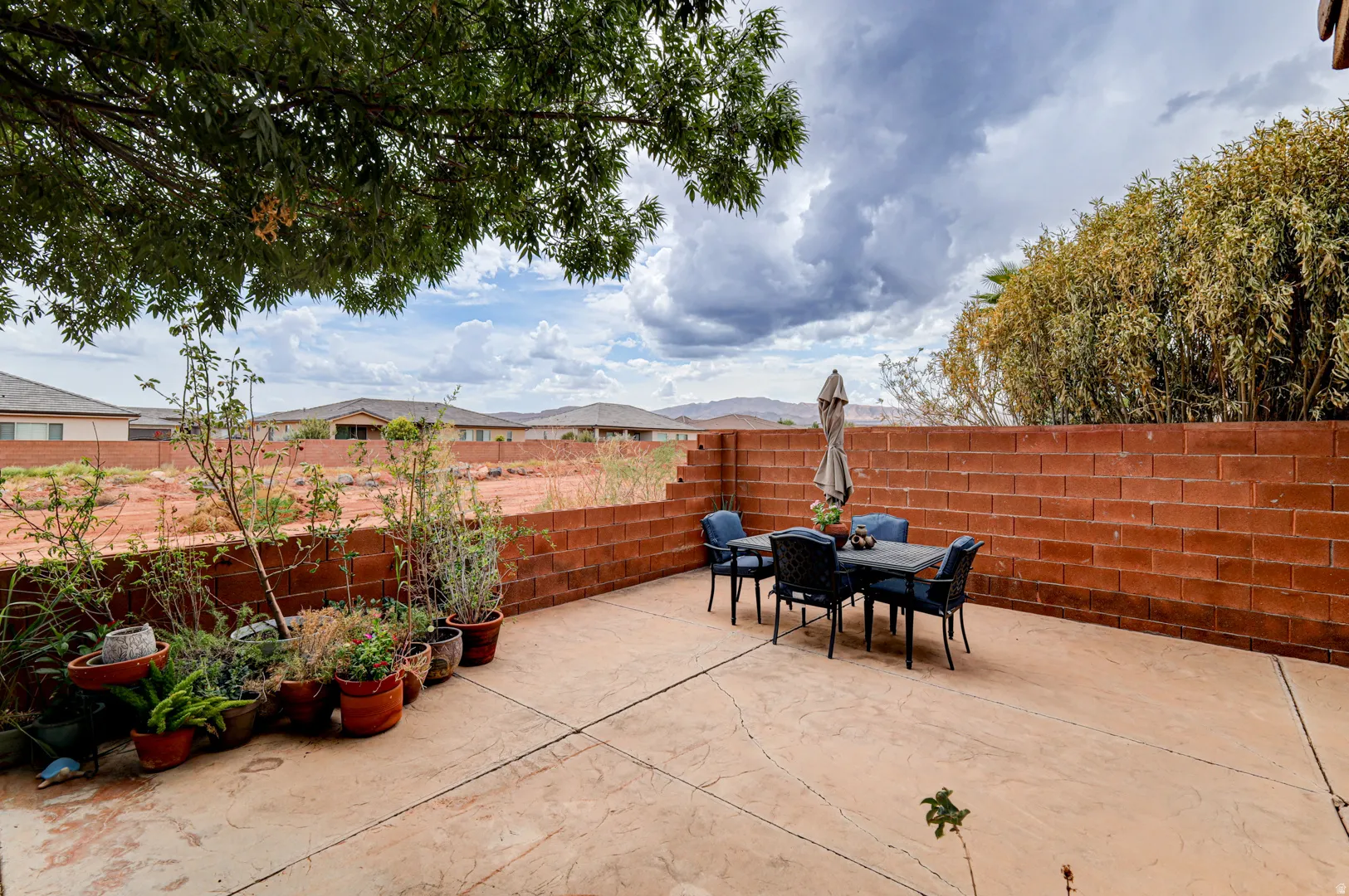 Concrete patio with a red brick privacy wall and mature trees