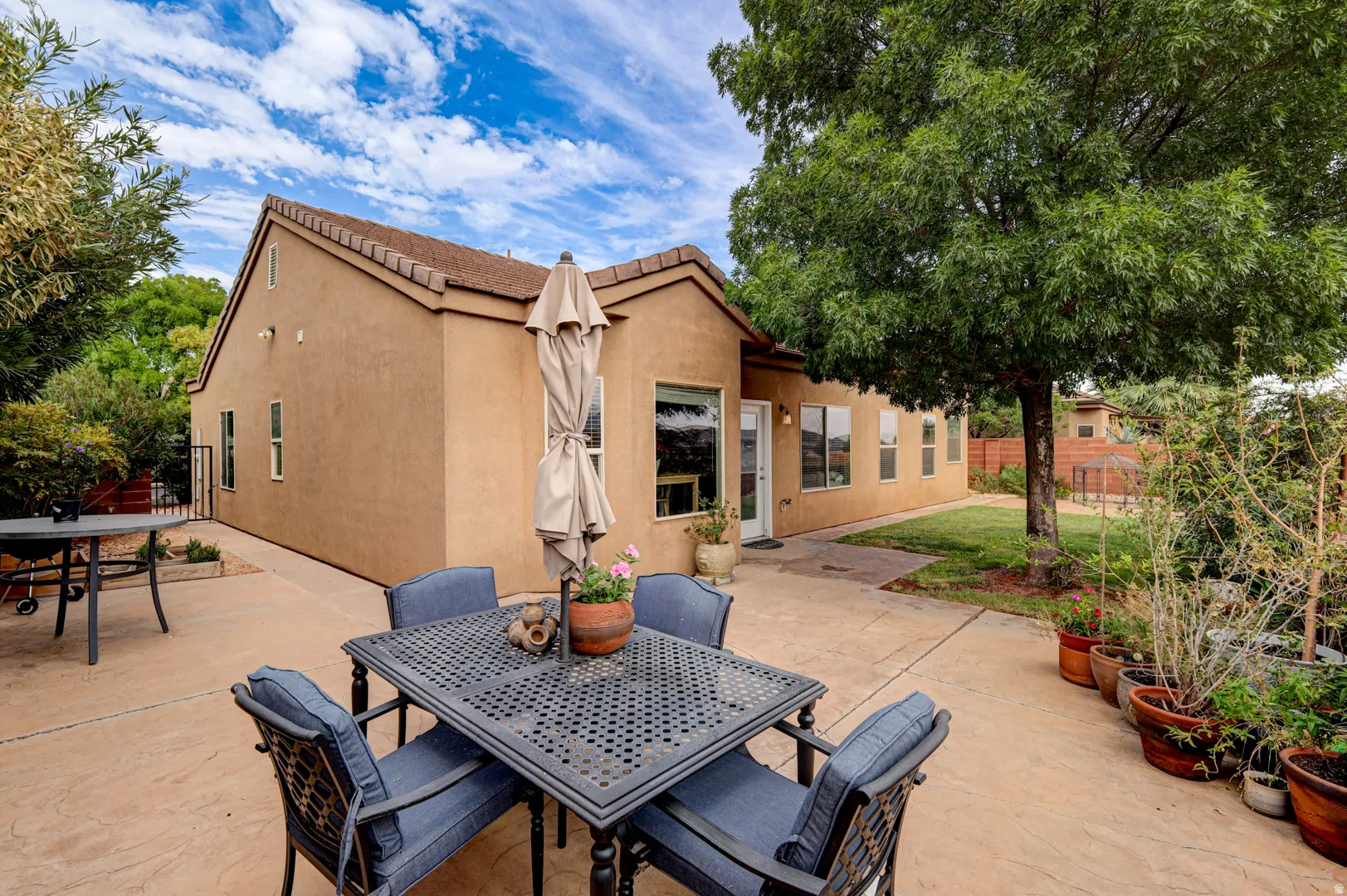 Exterior stucco finish with a tile roof, featuring multiple windows, a rear entry door, and an expansive stamped concrete patio