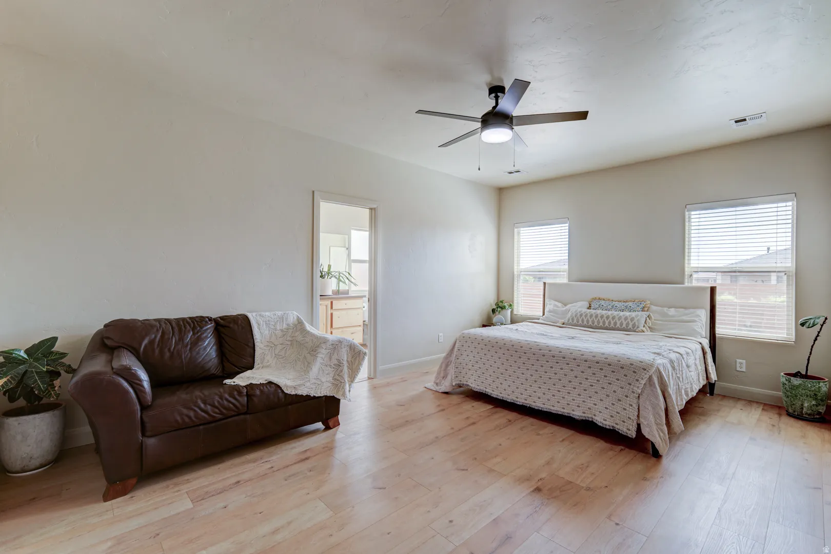 Light wood-finish flooring, two windows with blinds, and a ceiling fan with integrated lighting
