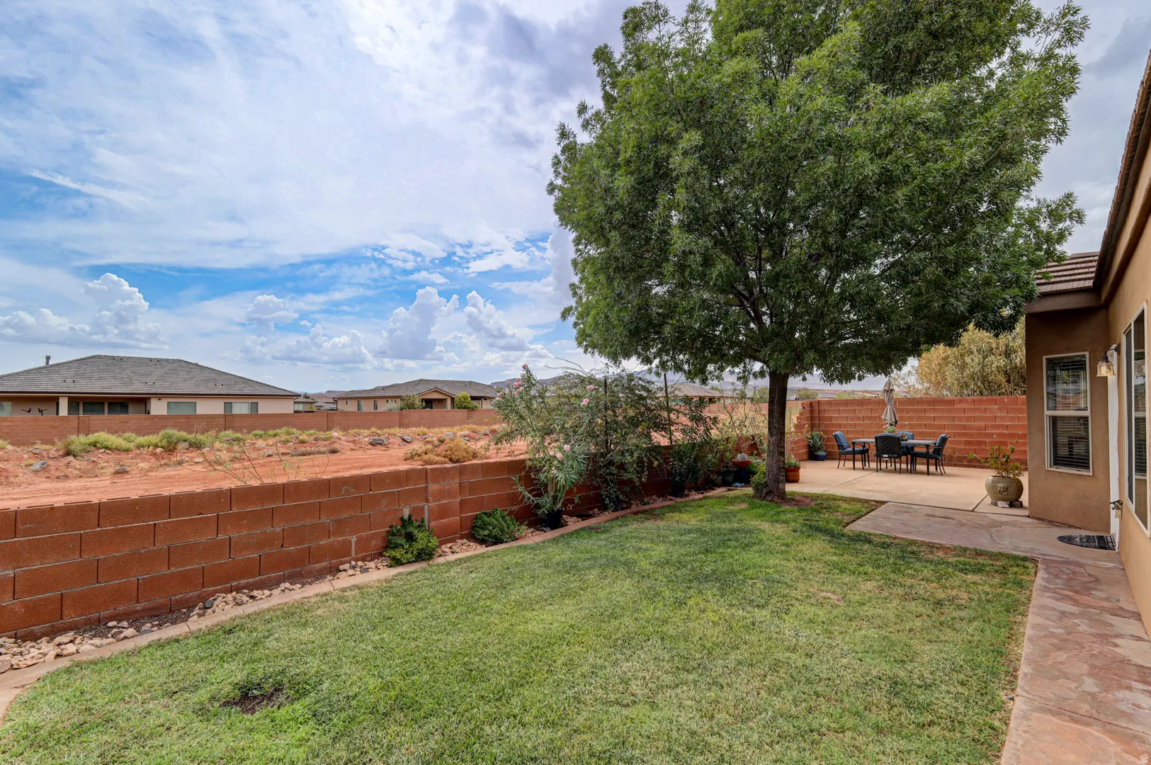 Expansive backyard featuring a manicured lawn, mature tree, and a large concrete patio