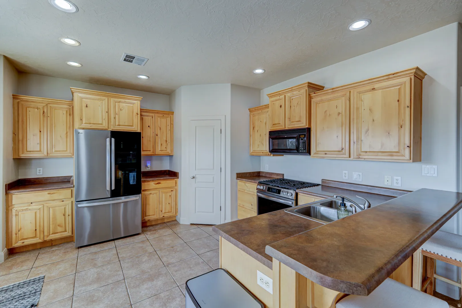 Kitchen with light wood-finish cabinetry, stainless steel appliances, and tile flooring