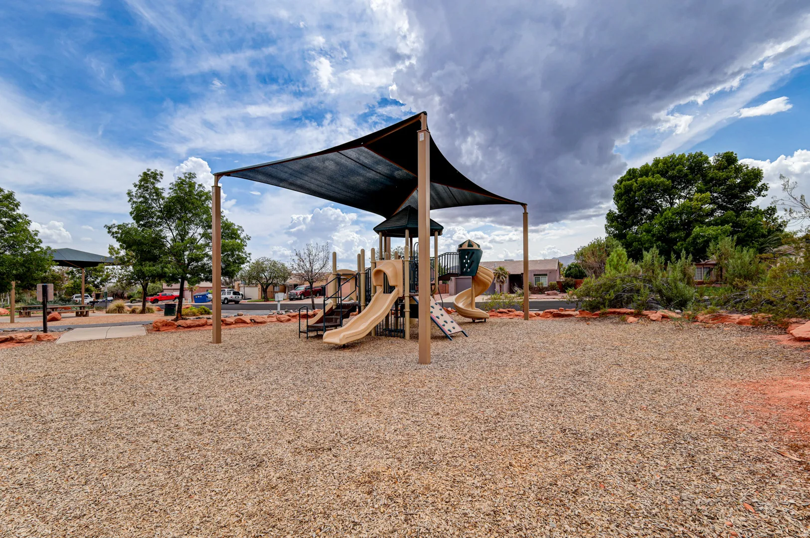 Playground featuring multiple slides, climbing structures, and shade canopies over a wood chip surface