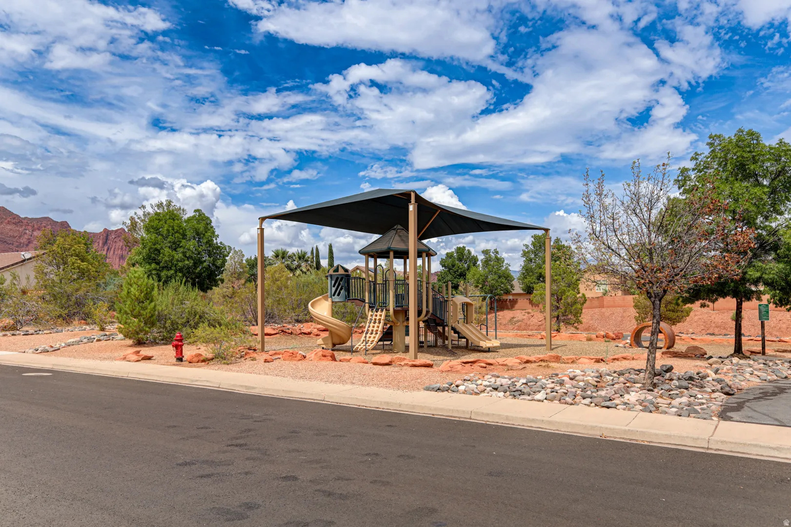 Playground area featuring a shade structure, multiple slides, and climbing elements on a gravel surface