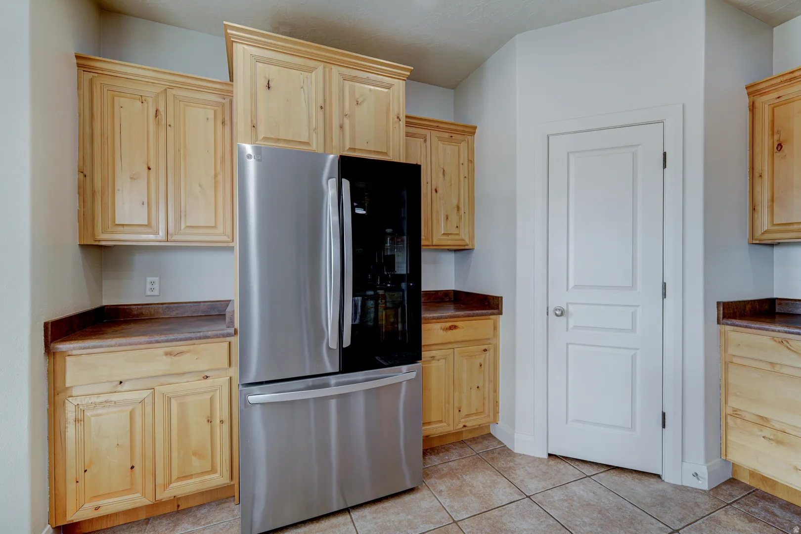 Light wood cabinetry with crown molding, dark countertops, tiled flooring, and a paneled interior door