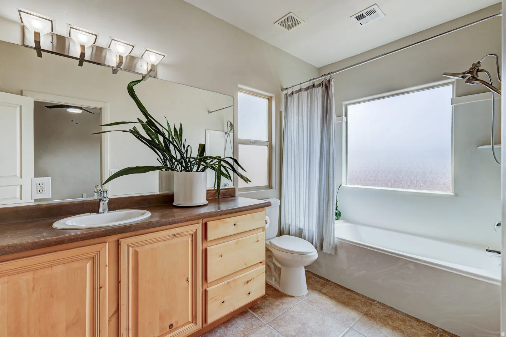 Bathroom featuring a dual-sink wood vanity with a single basin, a full-width wall mirror, and a bathtub with an integrated shower