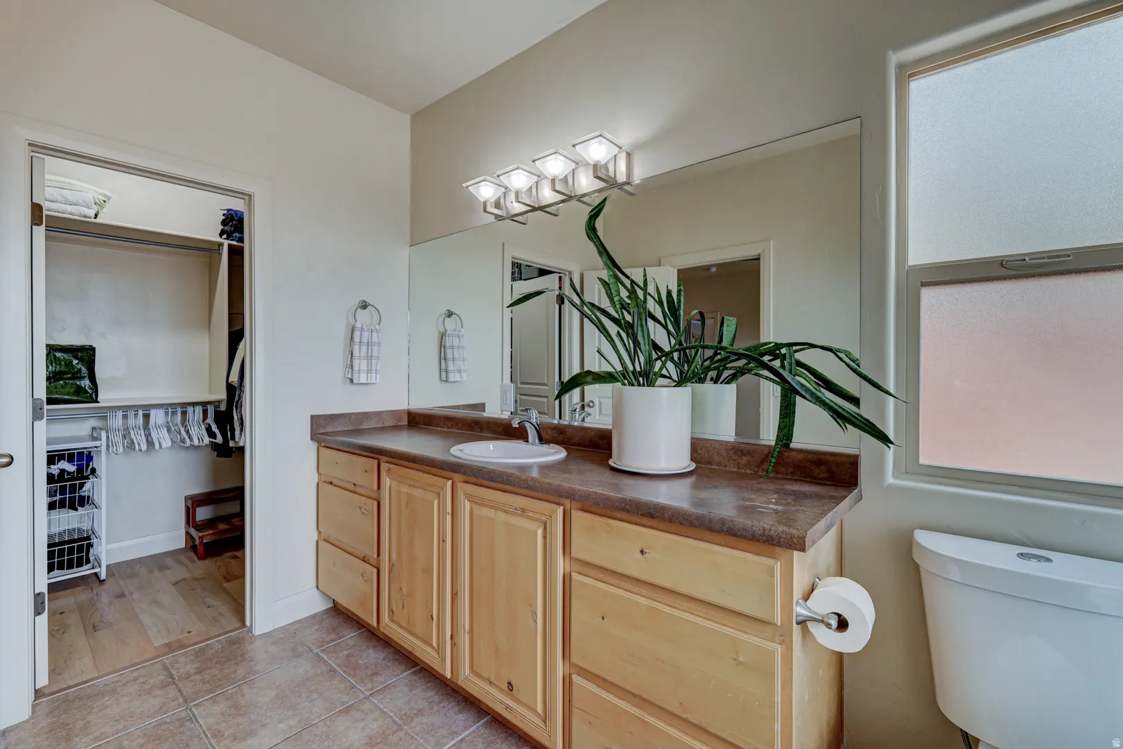 Bathroom featuring a vanity with a large mirror, wood-finish cabinetry, integrated sink, and tile flooring