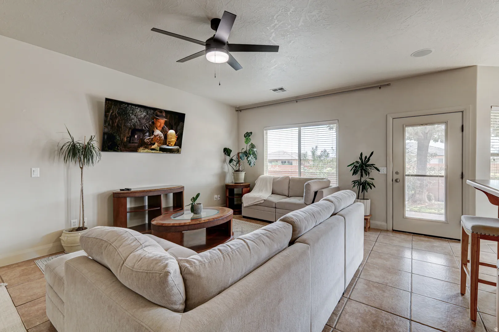 Living area with tile flooring, a ceiling fan with integrated lighting, and multiple windows with blinds