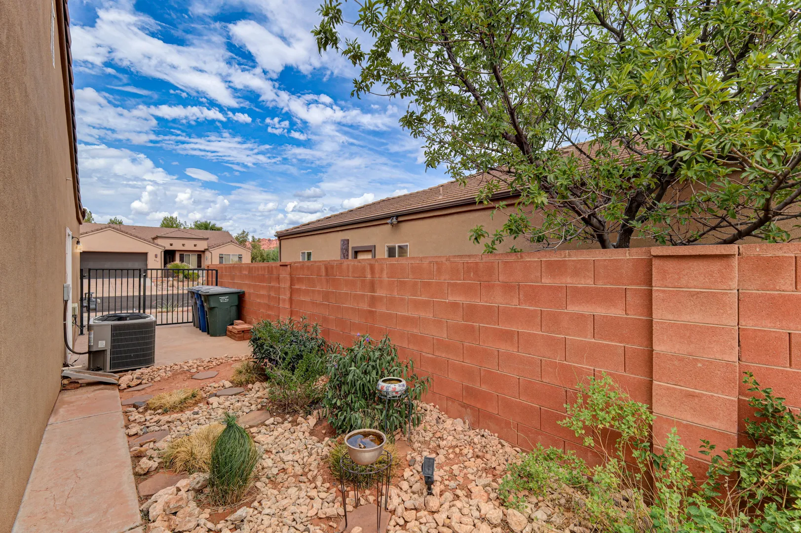 Enclosed side yard featuring a brick privacy wall, concrete pathway, decorative rock landscaping, and mature foliage