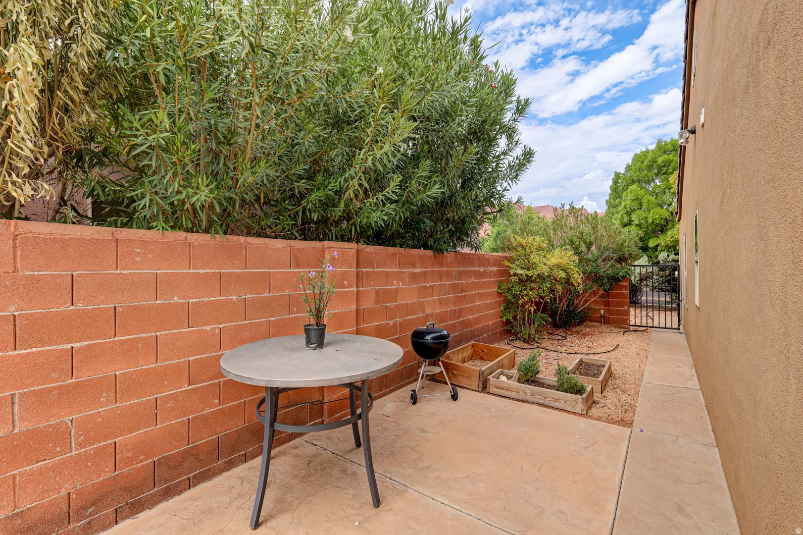 Private side patio with concrete hardscaping, a block privacy wall, and mature landscaping