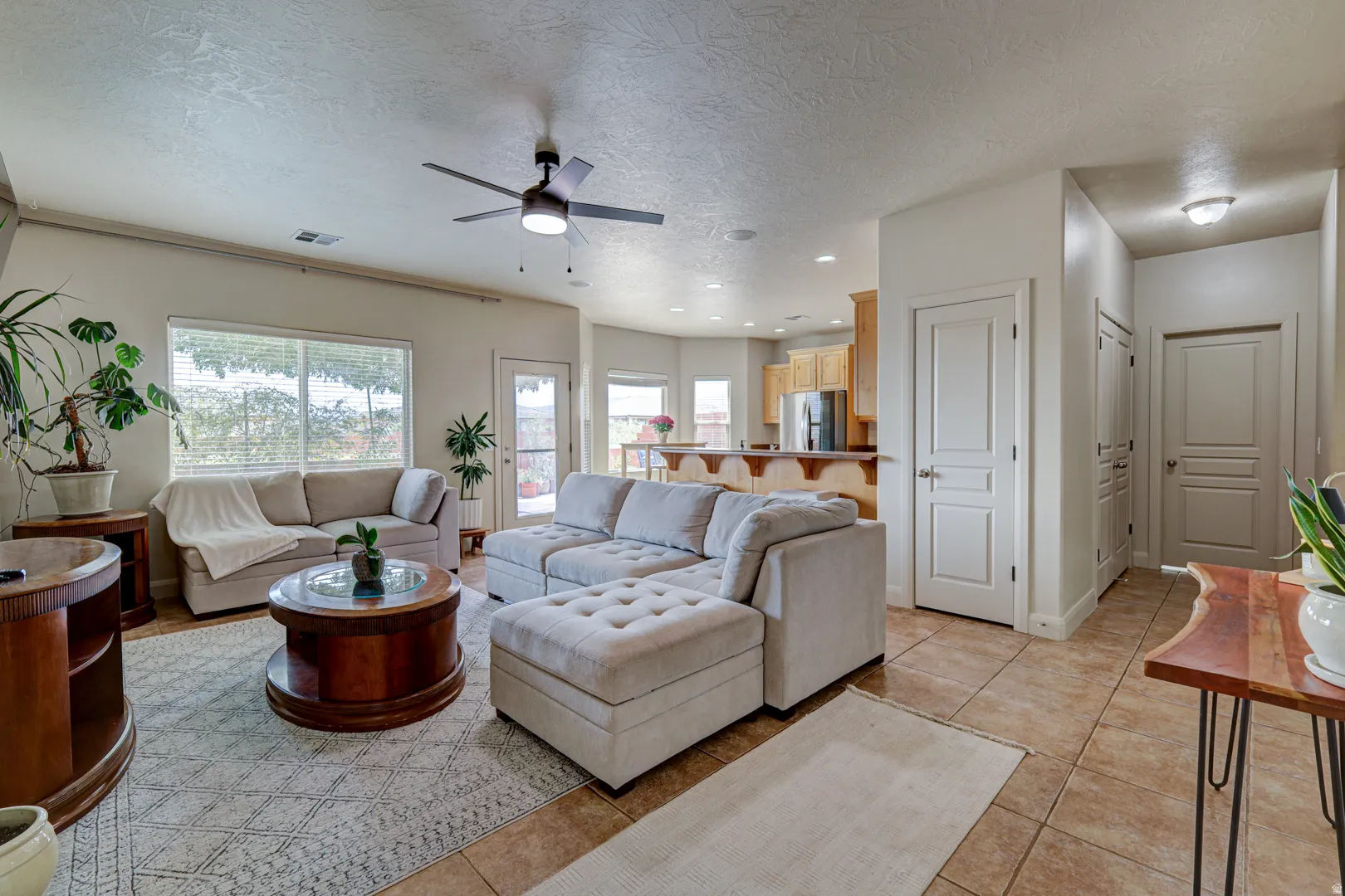 Spacious living area featuring tile flooring, a ceiling fan, and multiple windows
