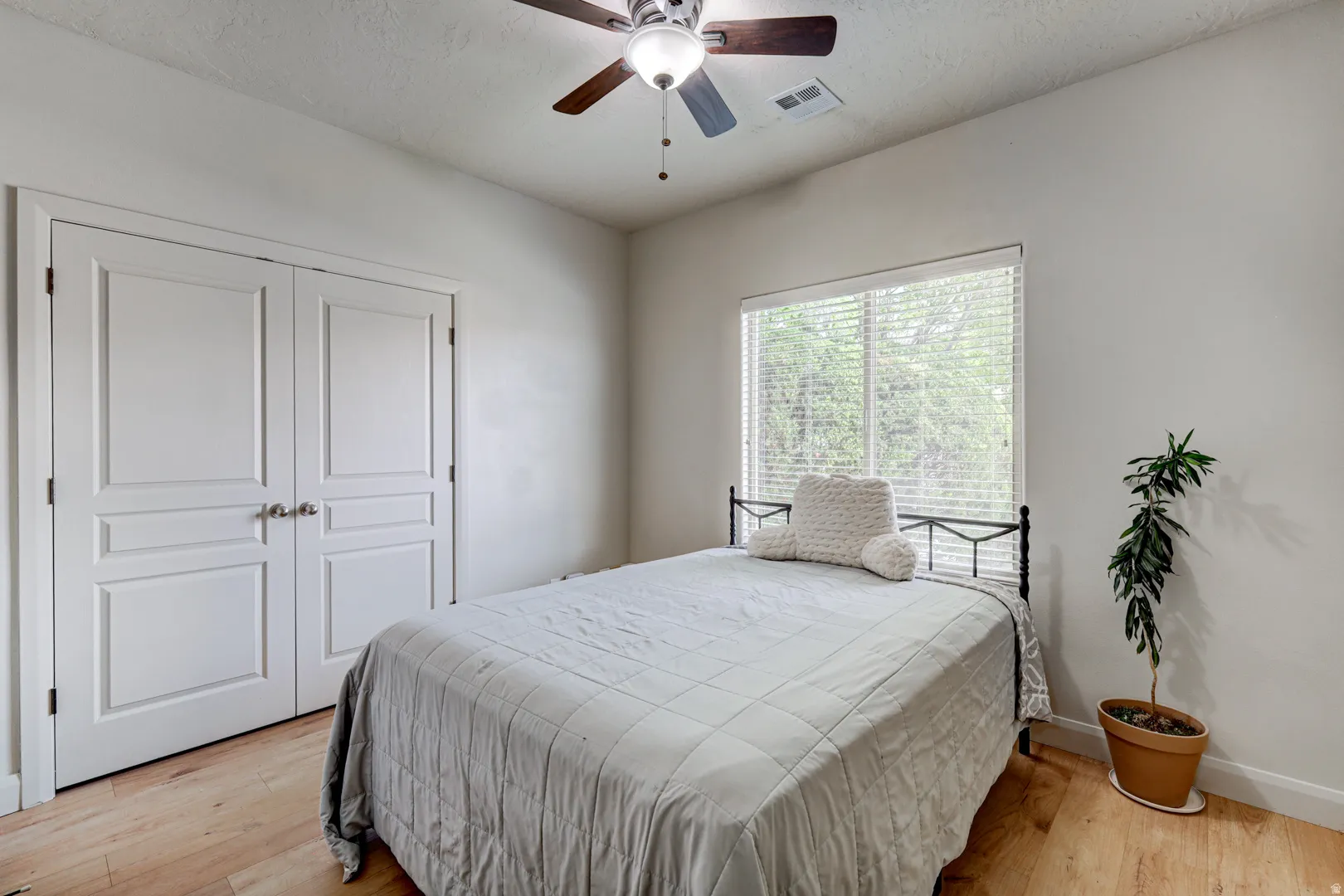 Wood-finish flooring, white paneled double doors, ceiling fan with integrated lighting, and a large window with horizontal blinds
