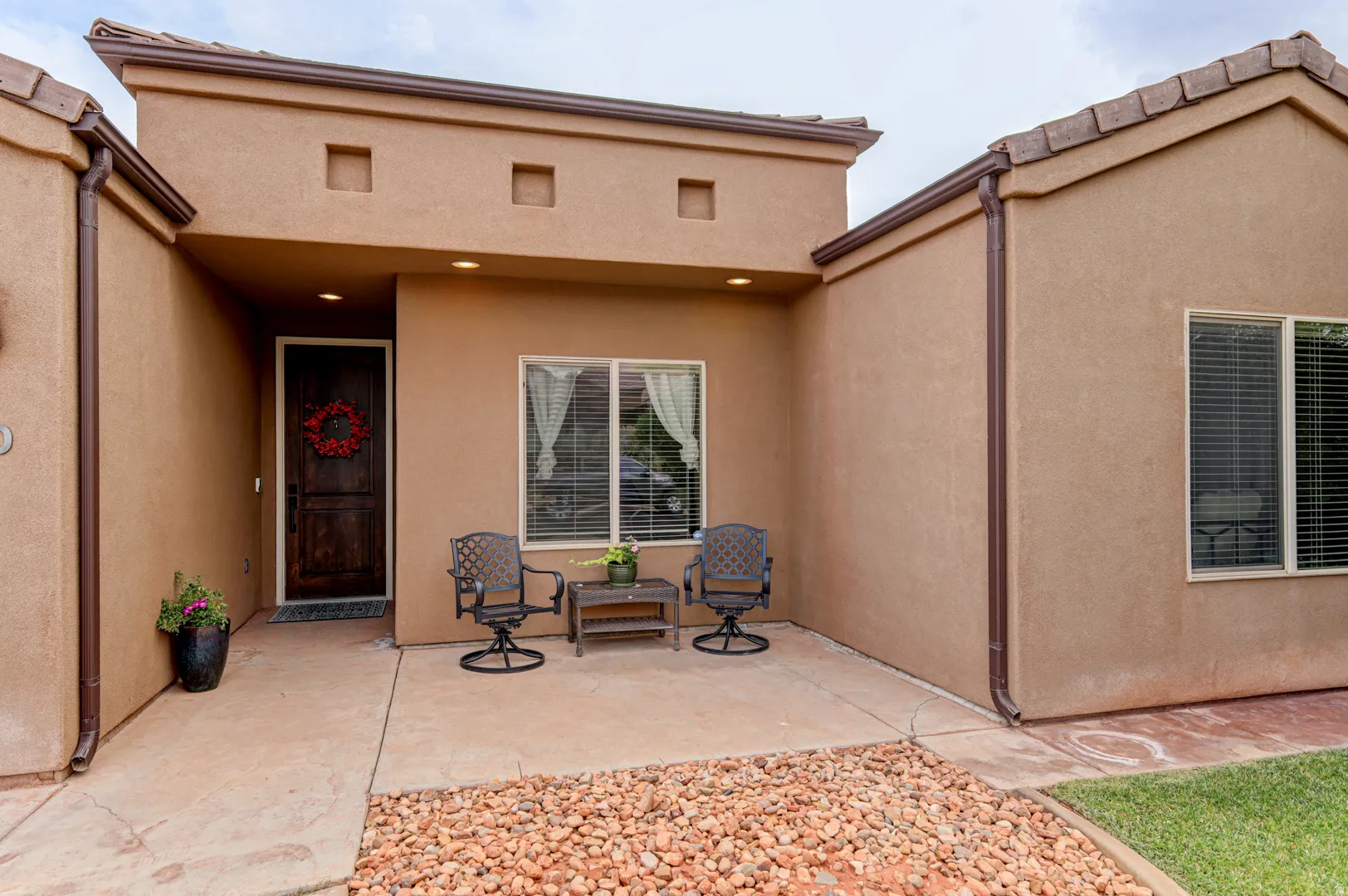 Stucco exterior with a covered entry, dark wood-finish door, and integrated recessed lighting