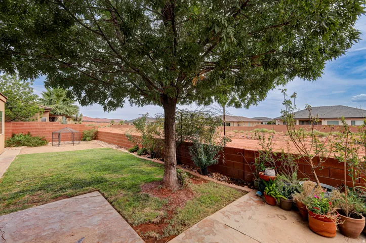 Grassed backyard area featuring a mature shade tree, a concrete patio, and a block wall perimeter