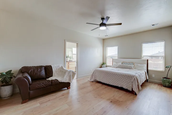 Light wood-finish flooring, two windows with blinds, and a ceiling fan with integrated lighting