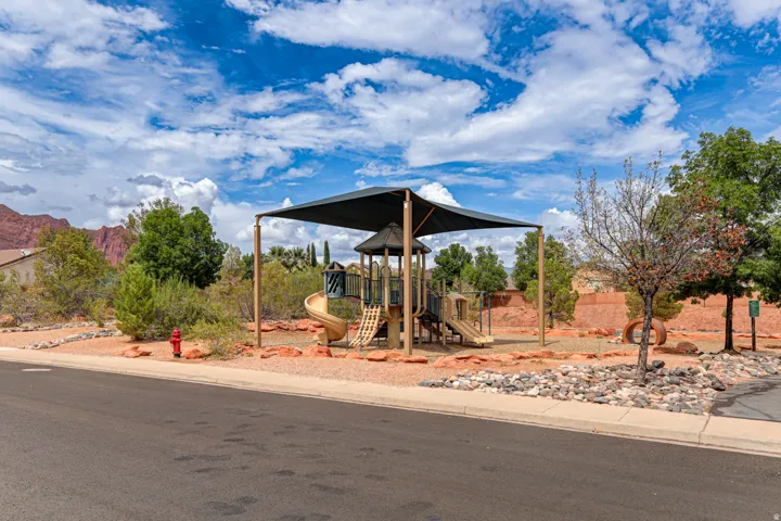 Playground area featuring a shade structure, multiple slides, and climbing elements on a gravel surface