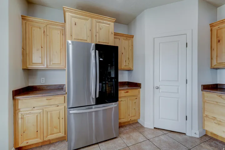 Light wood cabinetry with crown molding, dark countertops, tiled flooring, and a paneled interior door