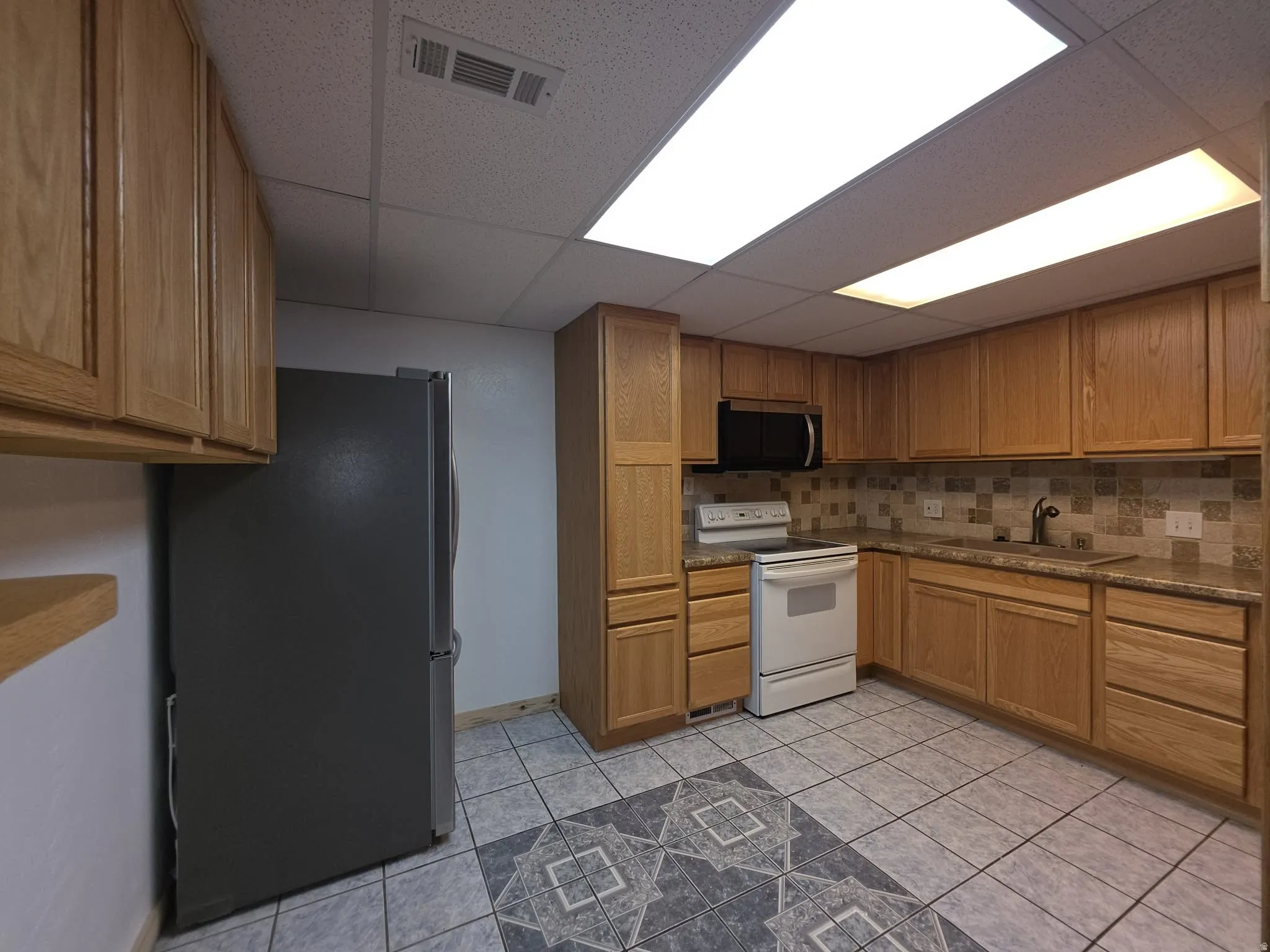 Kitchen featuring wood-finish cabinetry, tile flooring, stone-finish countertops, and a tiled backsplash