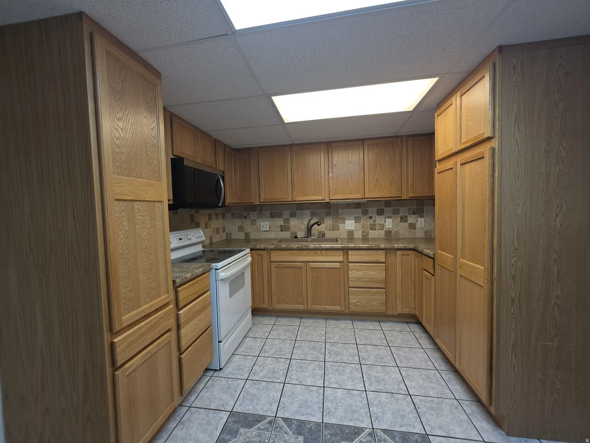 Kitchen featuring light wood-finish cabinetry, tile backsplash, laminate countertops, and tile flooring