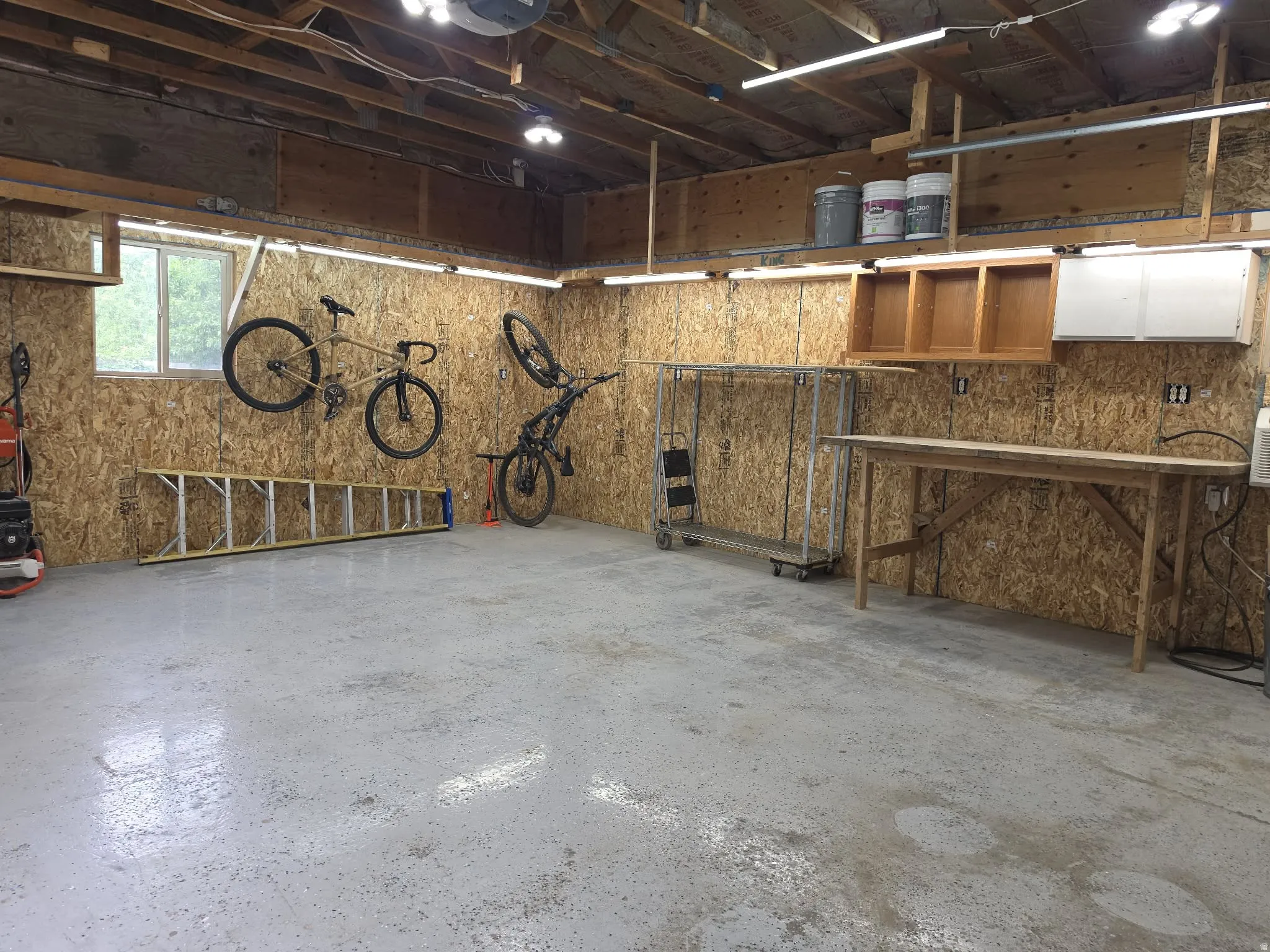 Concrete flooring, exposed wood beam ceiling, built-in shelving, wall-mounted cabinetry, and a workbench