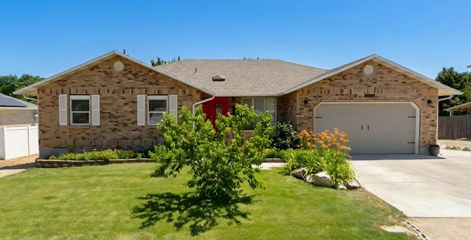Charming brick ranch home featuring a two-car attached garage, manicured front lawn with mature landscaping, and a gable roof with architectural detail