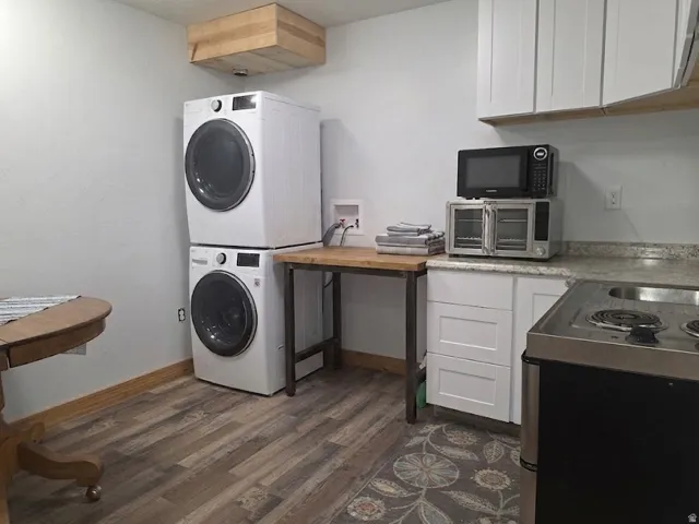 Stacked washer and dryer, wood-finish flooring, white cabinetry, integrated cooktop, and stone-finish countertop