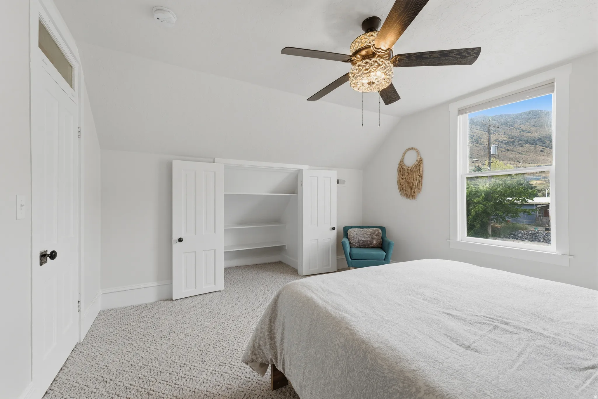 Vaulted ceiling with a contemporary ceiling fan, built-in shelving, white trim, and a window with mountain scenery