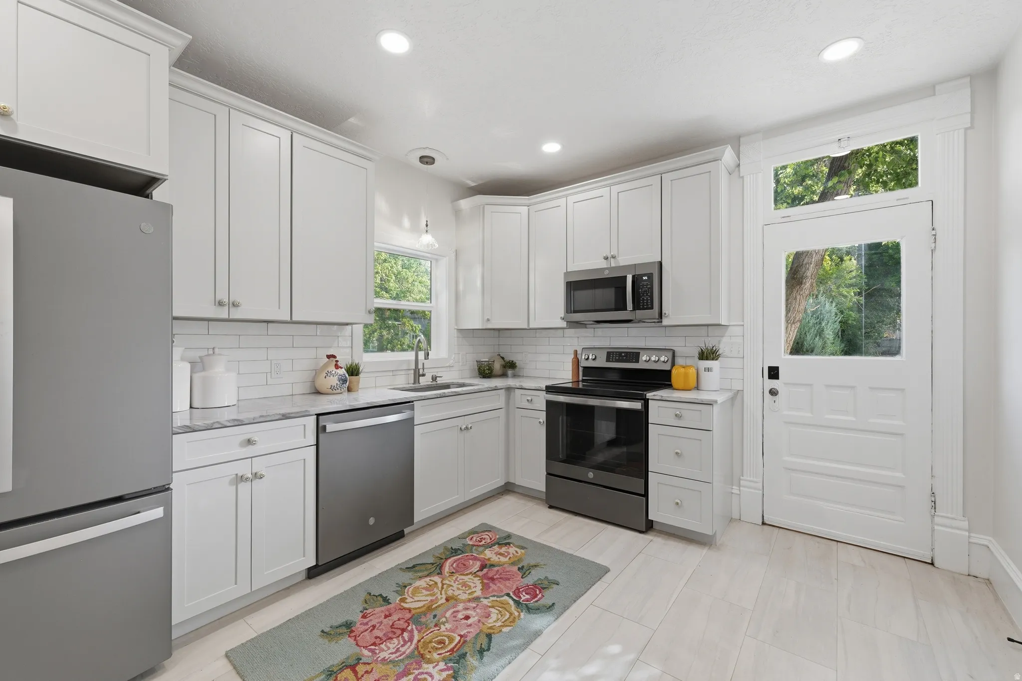 White shaker cabinetry, marble-finish countertops, subway tile backsplash, stainless steel appliances, and light wood-finish flooring