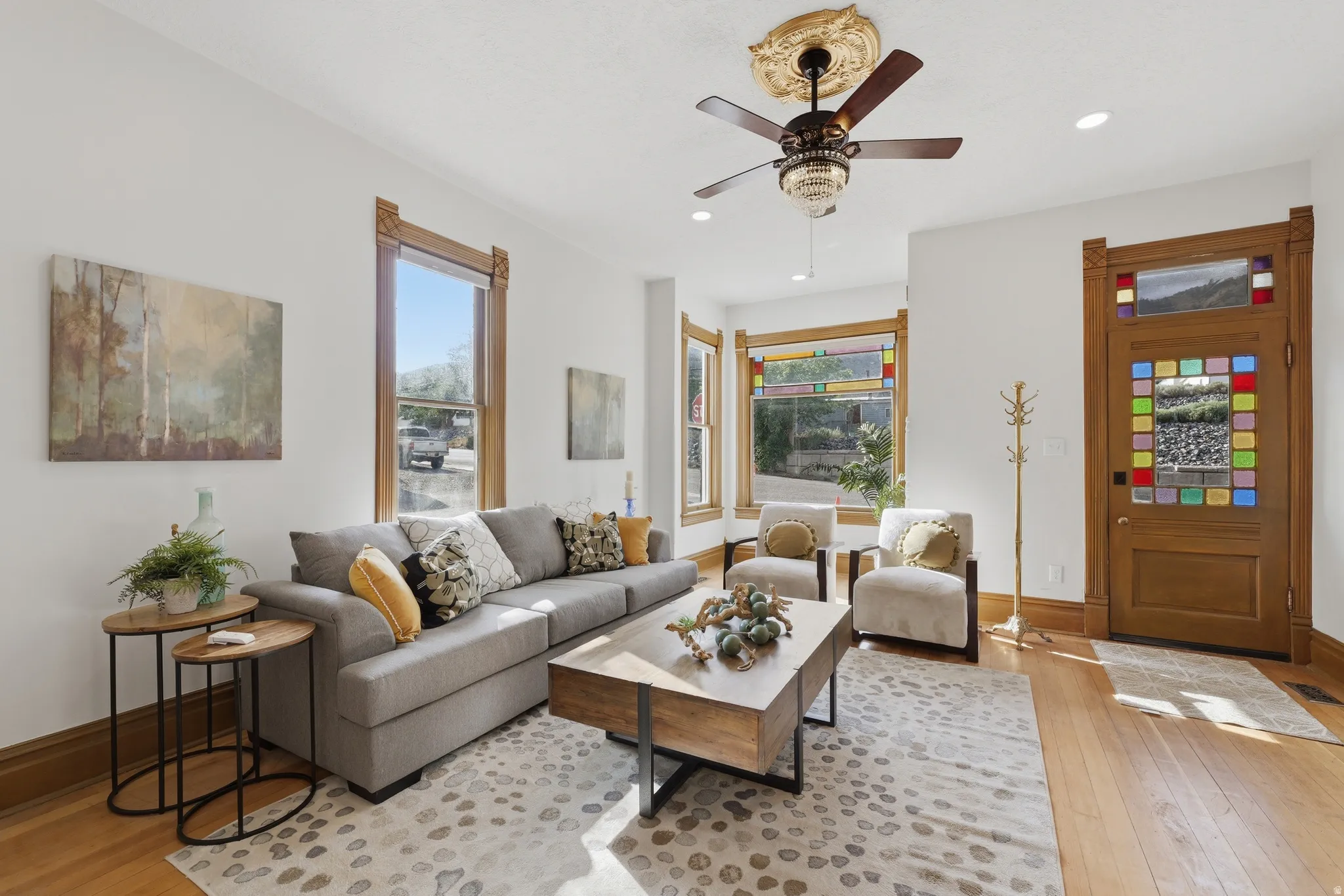 Hardwood flooring, decorative stained glass door, ornamental ceiling fan with light fixture, bay window, and detailed wood trim around windows and door