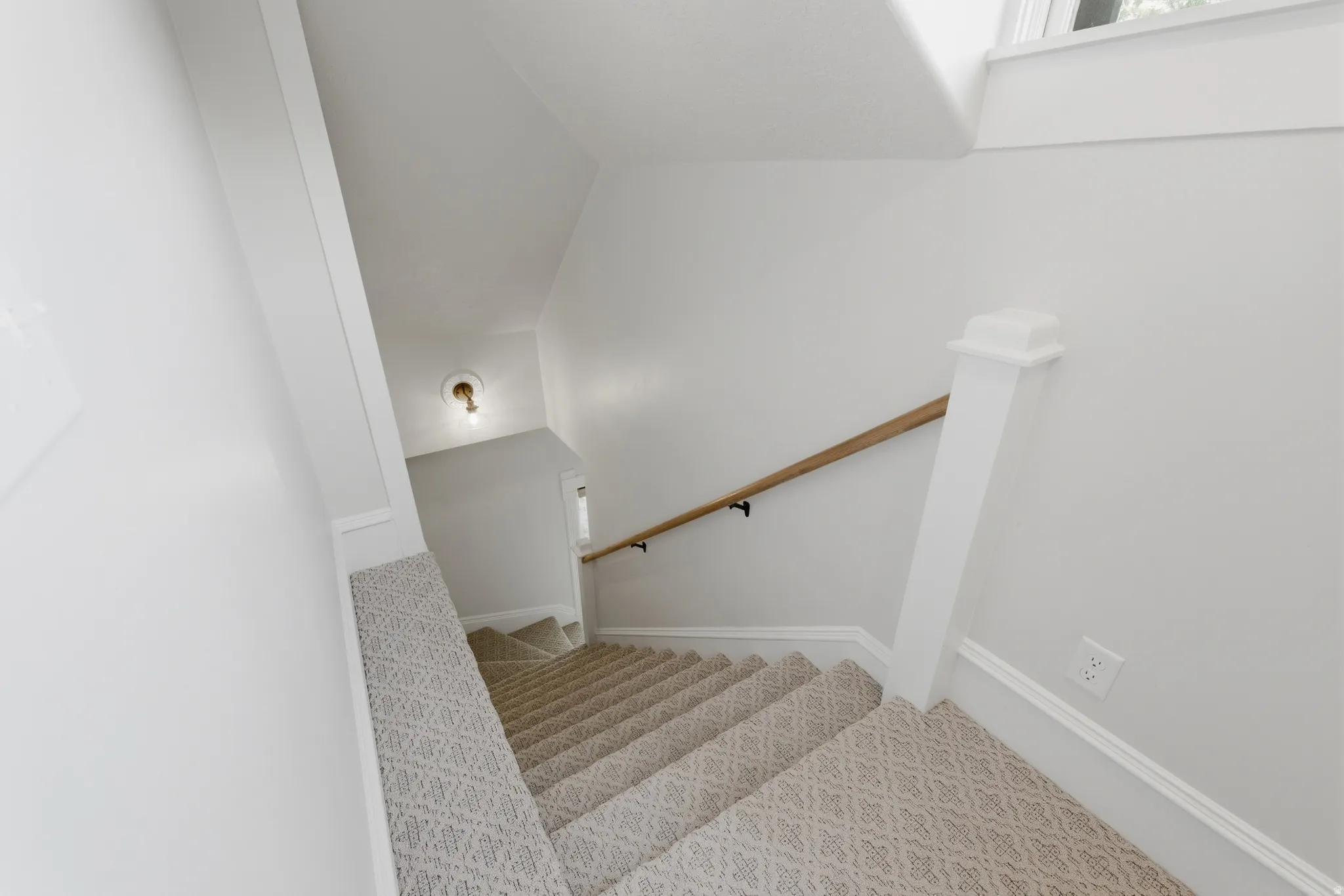 Staircase with patterned carpet, natural wood handrail, white newel post, and white trim
