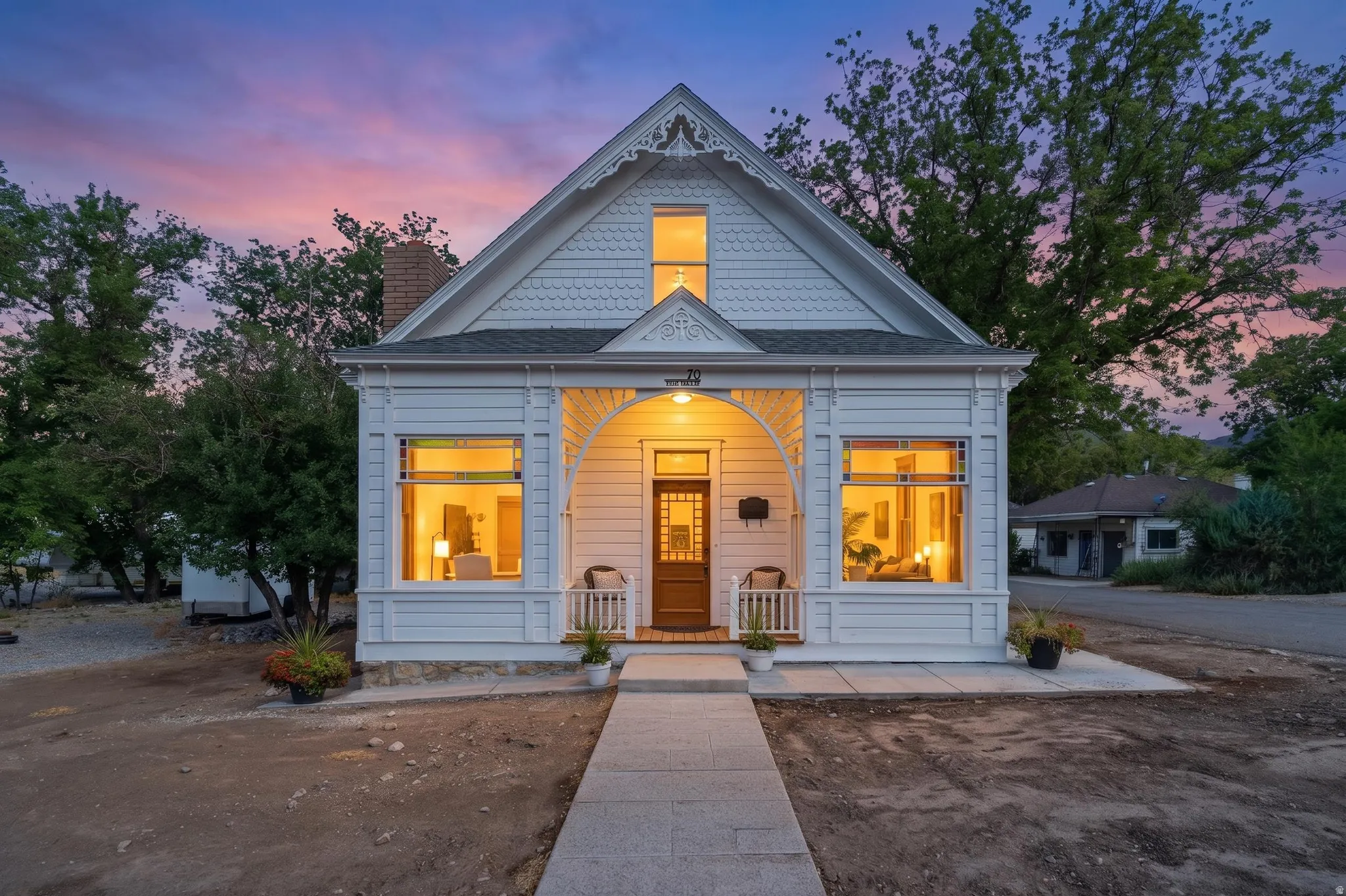 White exterior with intricate gable detailing, covered front porch, and a solid wood entry door