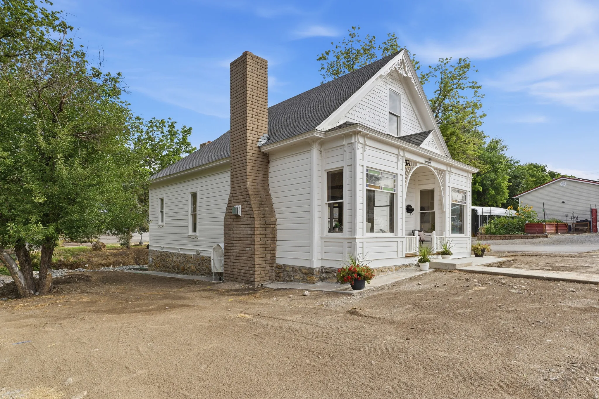 White siding exterior with a detailed covered porch, gable roof, and a prominent brick chimney