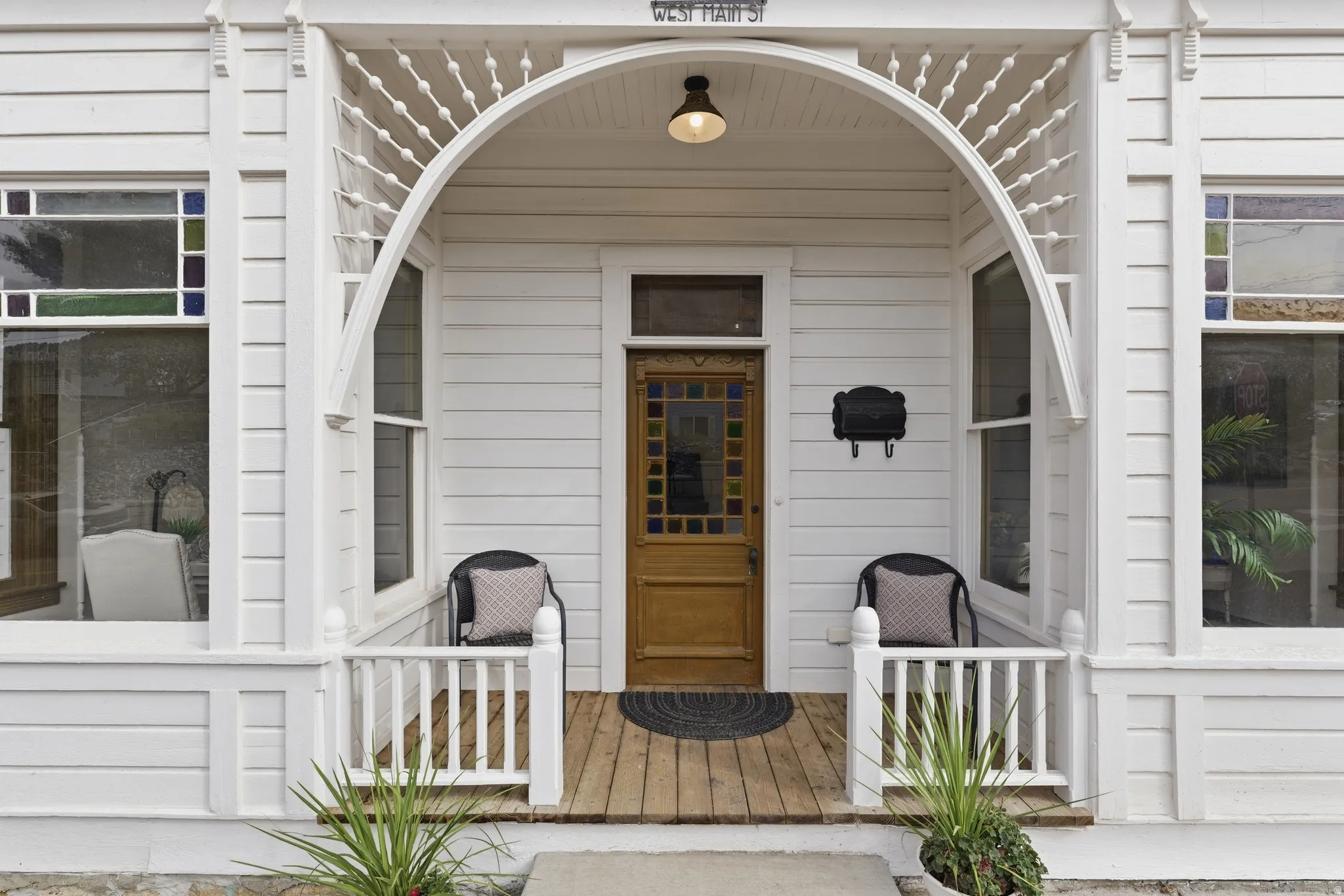 Crafted wooden entry door with stained glass accents, covered front porch, decorative spindle-work archway, and prominent white siding