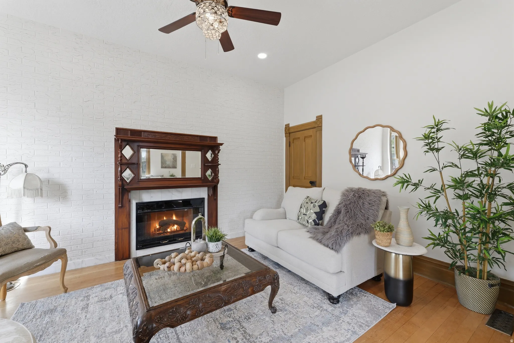 Hardwood flooring, white brick accent wall, wood-finish ceiling fan with crystal light fixture, built-in fireplace with wood mantel, and wood-finish trim work