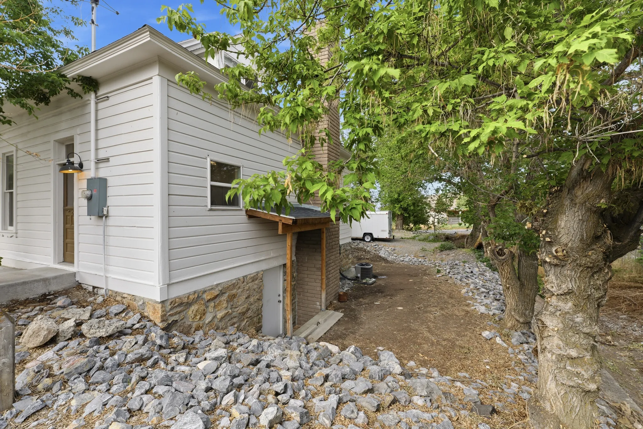 White horizontal siding exterior with stone foundation and mature trees